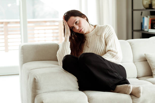 Woman sitting thoughtfully on sofa at home