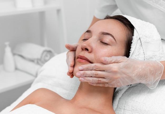 Woman Receiving Facial Treatment at Spa: A professional spa therapist wearing gloves is providing a relaxing facial massage to a calm woman lying