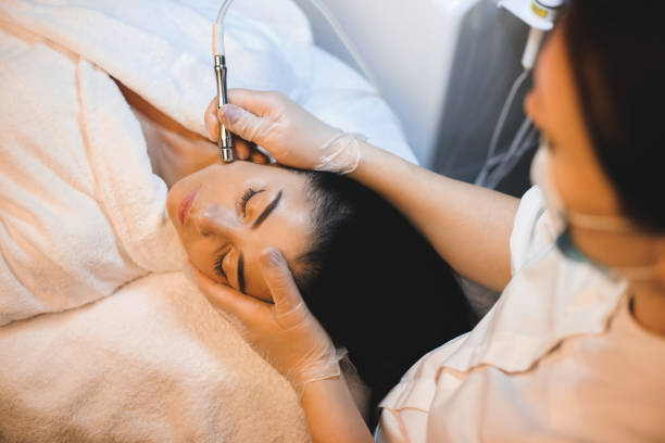 A woman receiving a facial treatment with a specialized tool in a spa setting, looking relaxed and comfortable while a beauty therapist works on